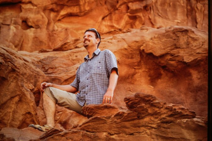 Mann auf rotem Sandsteinfelsen im Wadi Rum, lacht in die Sonne