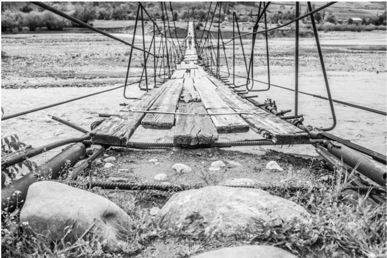 Wackelige Hängebrücke über einem Flussbett – sinnbildlich für das Reisen in Kirgistan
