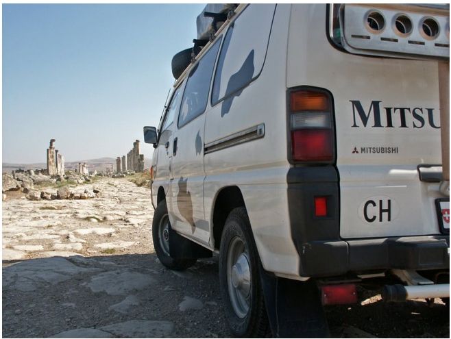 Mitsubishi-Bus mit CH-Schild vor antiken Ruinen in Syrien